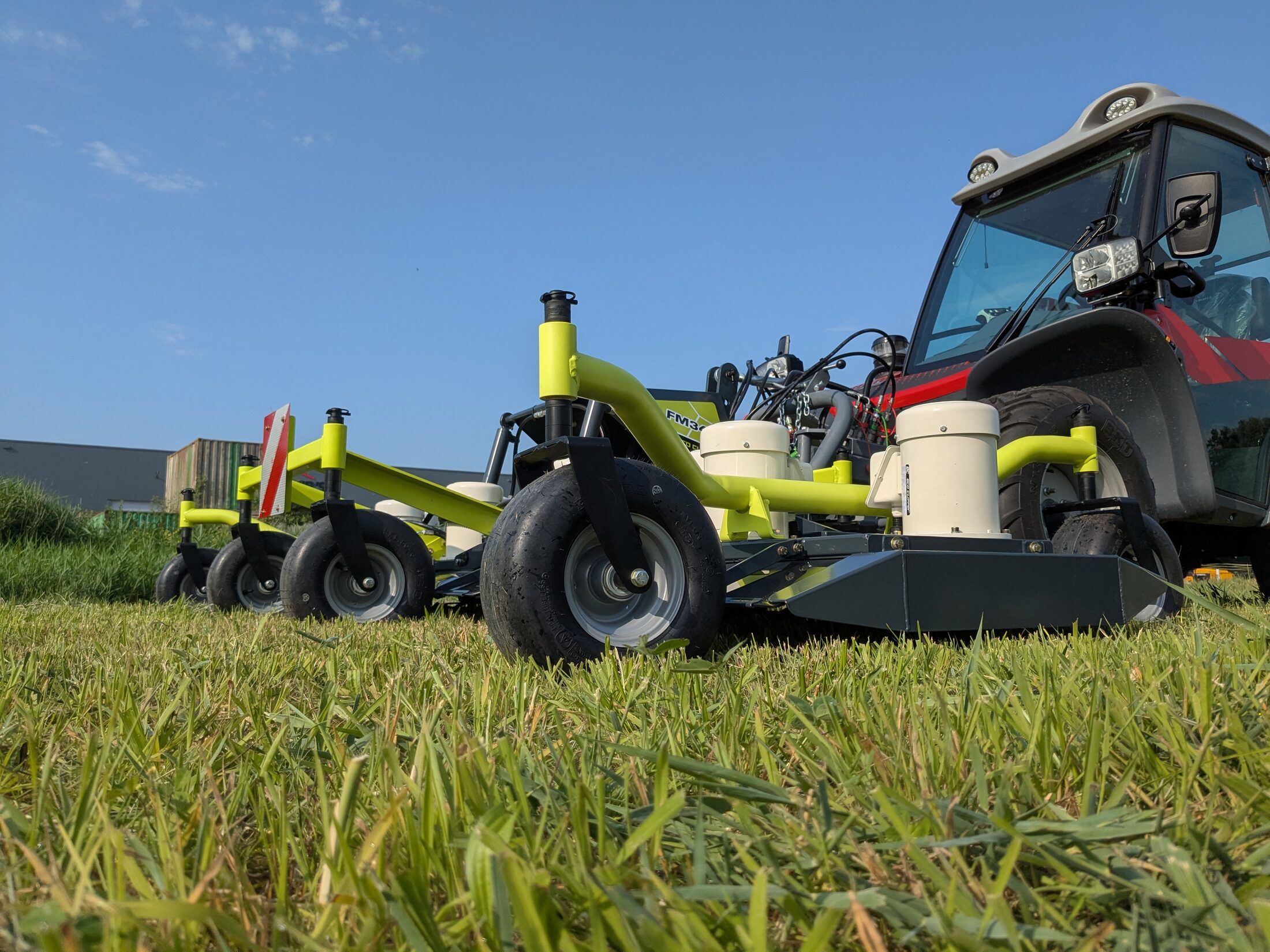Een felgroene Eco Clipper-maaier achter een trekker, laag bij het gras