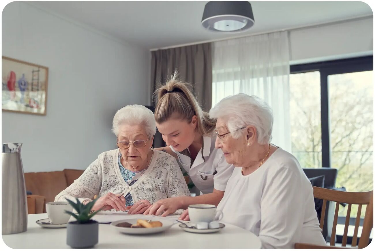 Een zorgverlener aan tafel met twee bewoners